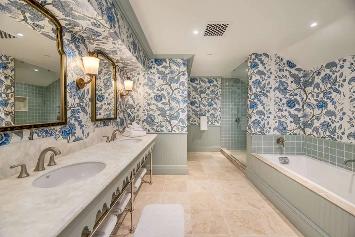 A luxurious bathroom adorned with floral wallpaper, a marble vanity, golden sconces, and a deep soaking tub. The space feels tranquil, spa-like, and perfect for moments of pure relaxation and self-care.