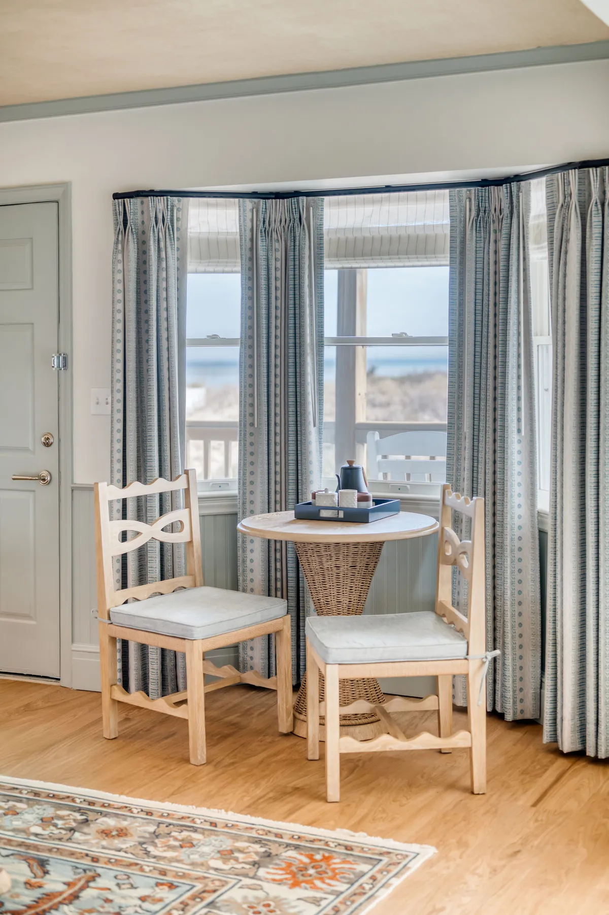 An inviting interior scene featuring a small round table and two wooden chairs beside a window, with decorative curtains framing a glimpse of the view outside. The setup is perfect for enjoying a sunrise coffee or a glass of wine while admiring the scenery.