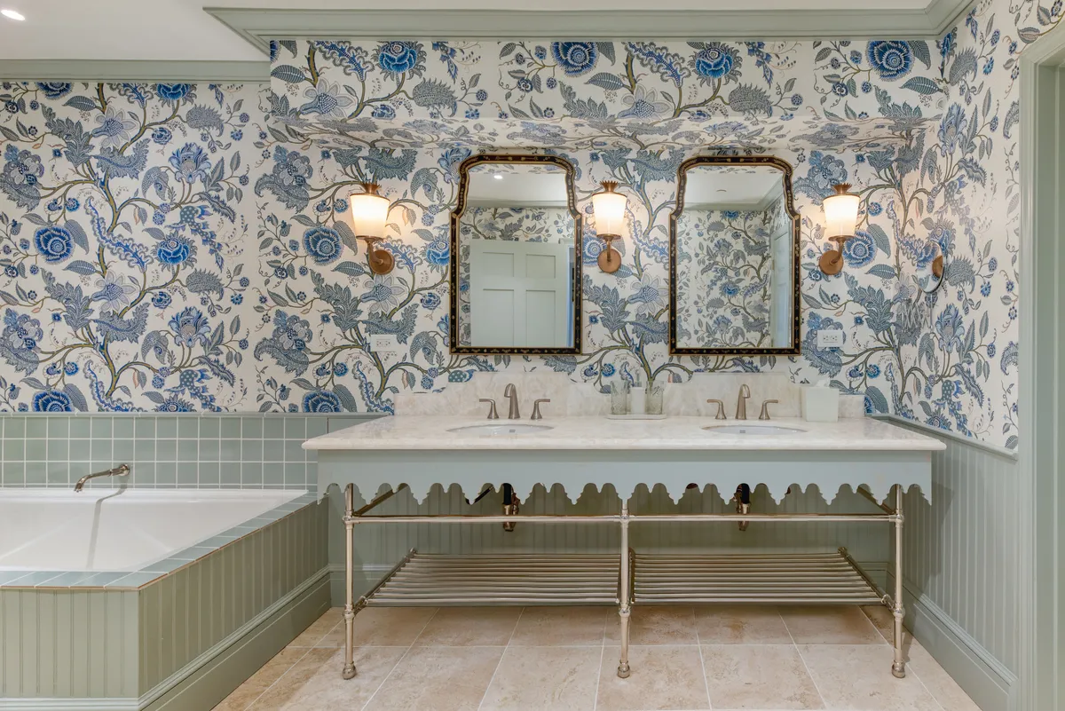 A beautifully appointed bathroom with floral wallpaper, double vanity mirrors, marble sink, vintage light fixtures, and a freestanding bathtub. The scene conveys a sense of wellness, luxury, and calm—ideal for self-care routines and enjoying organic bath amenities.