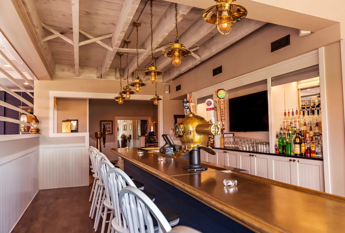 The image features a welcoming bar area with a sleek counter, stylish hanging light fixtures, and a well-stocked back bar filled with bottles. The mood is casual and sociable, inviting guests to gather, relax, and recount the day's adventures. The space radiates comfort and camaraderie, ideal for unwinding after an active day outdoors.