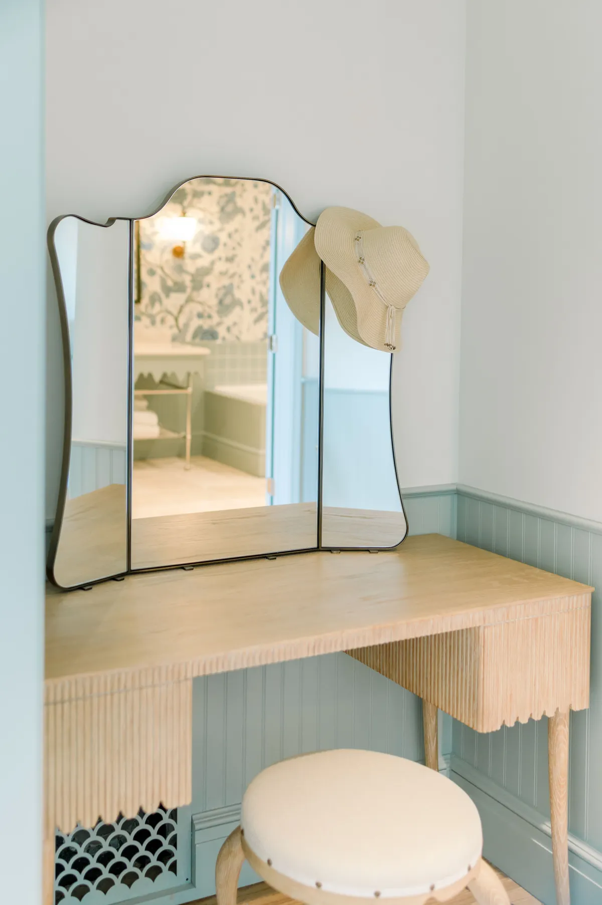 A bright vanity area with a wooden table, vanity mirror, and a hat resting on the mirror, creating a quiet and inviting nook for personal moments before heading out to explore.